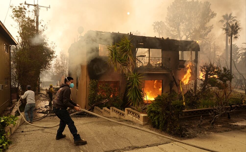 Personas ayudan a un bombero a estirar una manguera mientras un edificio de apartamentos se incendia, el miércoles 8 de enero de 2025, en la sección Altadena de Pasadena, California. Foto AP