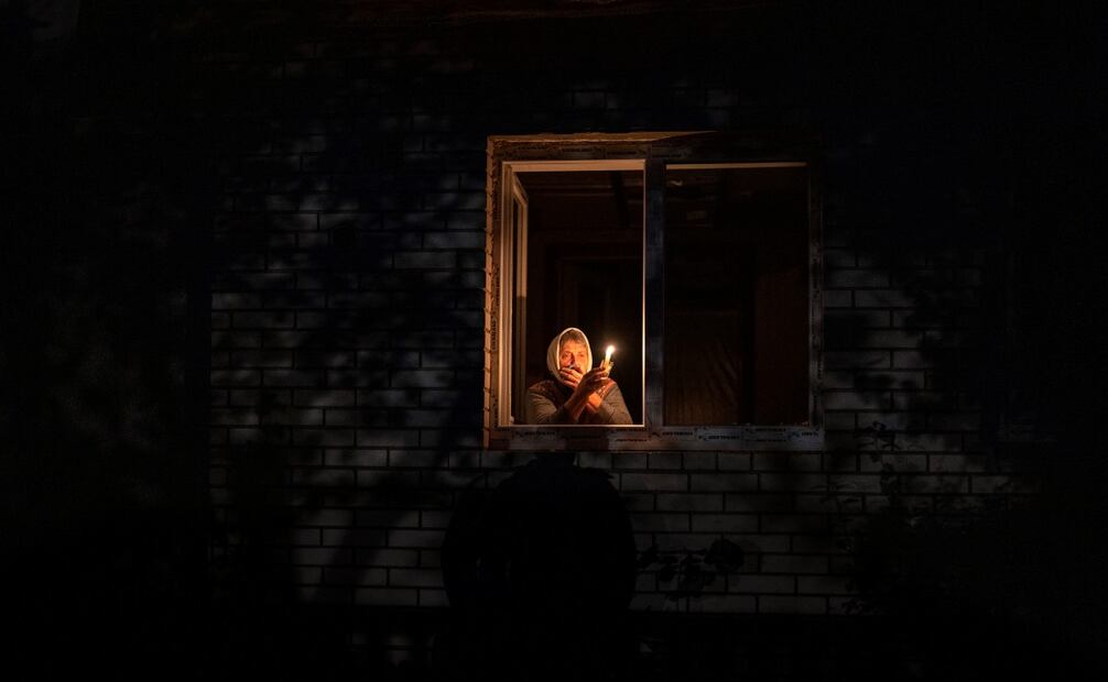 Catherine, de 70 años, mira por la ventana mientras sostiene una vela para iluminar el interior de su casa durante un apagón, en Borodyanka, en la región de Kiev, Ucrania, el 20 de octubre de 2022. Foto: AP